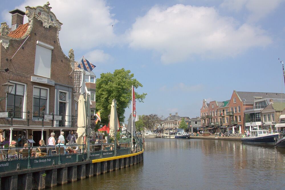 Terras met parasols en Friese vlag aan de kade in het centrum van Lemmer, met boten in het water en gevels aan de overzijde